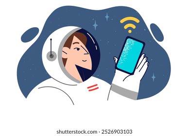 Woman astronaut holds smartphone while in space orbit, dressed in spacesuit and cosmonaut clothes. Girl astronaut uses wireless internet in mobile phone during cosmos expedition on spaceship.