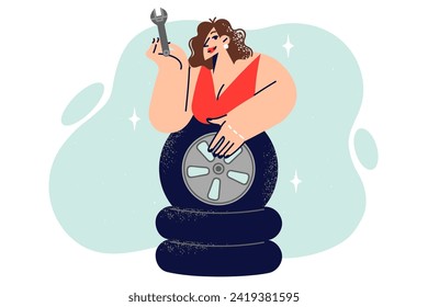 Woman auto mechanic leans over wheels and demonstrates wrench for self-repairing car. Girl in evening dress stands near tires for vehicle and needs help from mechanic from workshop.