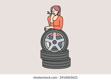 Woman auto mechanic prepares to replace car wheels during vehicle maintenance or repair. Happy girl auto mechanic with wrench in hands leans on tires, rejoicing at possibility replacing them on own