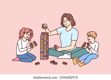 Woman babysitter together with kids plays constructor building tower of children blocks in kindergarten. Little boy and girl have good time and play educational games under supervision of babysitter