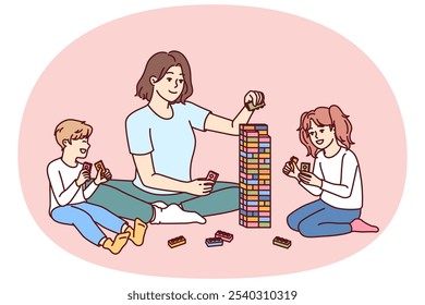 Woman babysitter together with kids plays constructor building tower of children blocks in kindergarten. Little boy and girl have good time and play educational games under supervision of babysitter