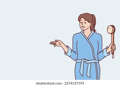 Woman in bathrobe holding shower brush in hand going to take bath and do self bodycare or anti-aging treatments. Positive girl after shower points to side, drawing your attention to importance hygiene