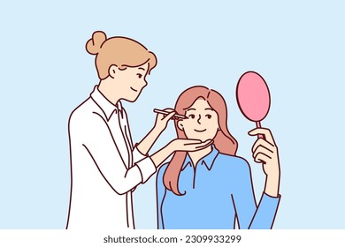 Woman beautician makes make-up of patient with mirror undergoing aesthetic treatment in medical clinic. Girl make-up beautician applies makeup on face of actress before filming movie or going on stage svg