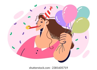 Woman in birthday hat holds balloons and stands among falling confetti during anniversary party. Girl with birthday tongue in mouth celebrates day of angel and invites you to come to banquet.