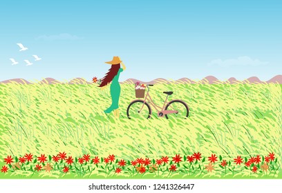 Woman in blue skirt wearing a hat with a bicycle standing in a field with reed flowers, the sky and mountains as the background.