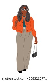 A woman in a bright orange jacket and tan pants is walking down the street. She is holding a black purse and wearing sunglasses. The image has a bright and cheerful mood, with the womans outfit