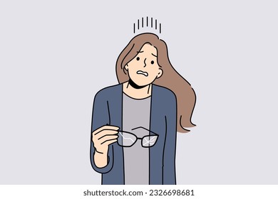 Woman with broken glasses in hands makes confused face not knowing how to solve vision problem. Careless girl holds glasses with cracked glass and needs to go to optometrist or buy contact lenses