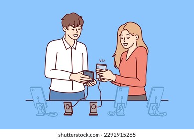 Woman buys new mobile phone in consultation with employee of digital gadget store. Man and girl are standing near showcase with smartphones connected by wire to counter, to avoid stealing phone 