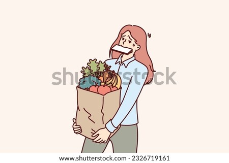 Woman carries shopping bag and holds phone in mouth after returning from grocery market with organic food. Girl bought lot of healthy food and is trying to bring organic vegetables and fruits on own