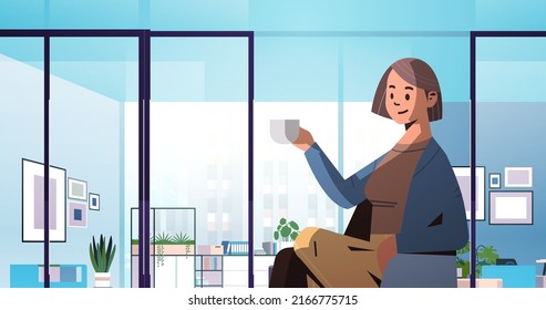 woman in casual clothes sitting on chair and drinking coffee businesswoman relaxing in armchair office interior