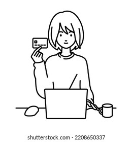 a woman in casual style using laptop computer at her desk and holding a credit card with a mug