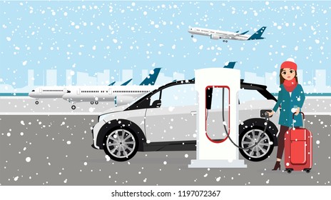 Woman charges an electric car at a charging station for electric vehicles. Winter time. Snow.