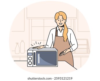 Woman cook demonstrates new microwave oven for heating cold food and drinks. Girl chef stands in kitchen of cafe or dining room and points with hand at microwave oven for hot lunch processing