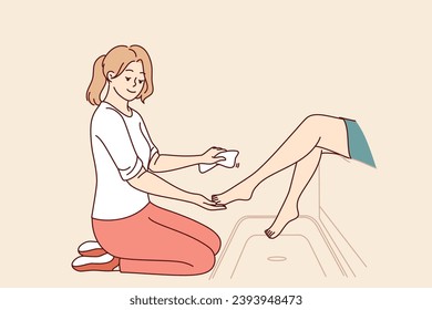 La cosmetóloga femenina da pedicura al cliente mientras se sienta de rodillas y trata las piernas del paciente con crema suavizante. Chica sonriente trabaja en un salón de belleza y aprende a hacer pedicura para las visitantes femeninas