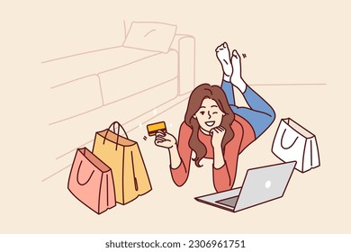 Woman with credit card and laptop after internet shopping or ordering goods on website of popular online store. Girl lying on floor and winking invites to shopping using bank card with cashback