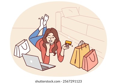 Woman with credit card and laptop after internet shopping or ordering goods on website of popular online store. Girl lying on floor and winking invites to shopping using bank card with cashback