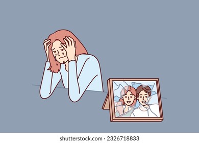 Woman cries after breaking up with husband and is sad sitting near broken photo with happy family. Widow girl cries and sheds tears after death of boyfriend causing emotional distress.