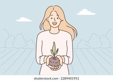 Woman demonstrates handful of soil with young plant for concept of caring for nature and celebrating earth day. Happy woman who wants to go into gardening or farming business stands on plantation 