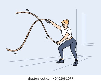 Woman doing fitness using battle rope training at sport center to lose weight or build muscles. Girl athlete with battle rope prepares for competitions and leads healthy lifestyle.