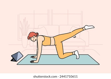 Woman doing fitness watching online lesson from trainer, doing stretching on sports mat in living room. Girl is interested in fitness and health-improving gymnastics, thanks to webinars from internet.