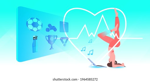 woman doing sport exercises in salamba sirsasana pose while watching video fitness on laptop online training
