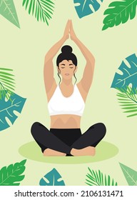 Woman doing yoga in lotus position against the background of tropical leaves and flowers