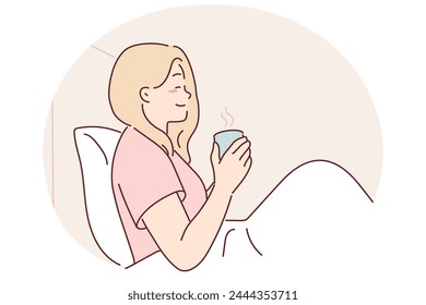 Woman is drinking coffee sitting in bed under blanket enjoying morning weekend and good mood. Girl with mug of coffee has breakfast in bedroom, drinks invigorating drink to wake up faster and smiles