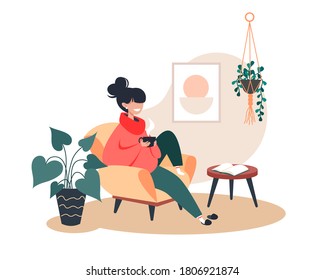 Woman drinking hot tea while sitting in armchair in cozy room