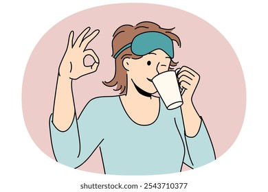 Woman drinks morning coffee after waking up and shows ok gesture standing in sleep mask and pajamas. Girl winks enjoying hot coffee or tea drink to cheer up and get ready for work day