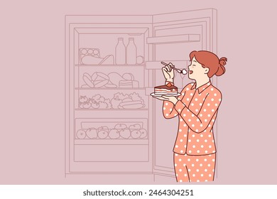 Woman eats cake at night, standing in pajamas near open refrigerator and risking becoming overweight. Concept of eating cholesterol cake due to lack of willpower to follow diet causing diabetes