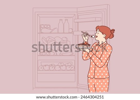 Woman eats cake at night, standing in pajamas near open refrigerator and risking becoming overweight. Concept of eating cholesterol cake due to lack of willpower to follow diet causing diabetes
