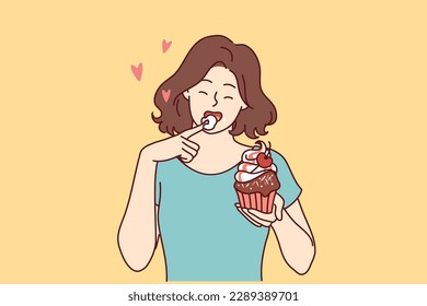 Woman eats delicious cupcake, licking sweet cream from finger and enjoying appetizing dessert bought in craft bakery. Beautiful girl having lunch with cupcake with fresh berries from cake shop 