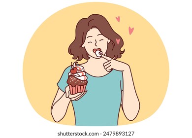 Woman eats delicious cupcake, licking sweet cream from finger and enjoying appetizing dessert bought in craft bakery. Beautiful girl having lunch with cupcake with fresh berries from cake shop