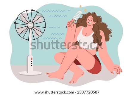 Woman eats ice cream and sits on floor near electric fan, cooling off during sudden warming of summer. Girl relaxes and laughs, cooling off after returning from walk along hot street