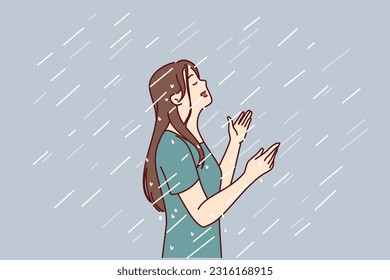 Woman enjoys rain standing under drops falling from sky in wet t-shirt and raising head up. Happy young girl rejoices in autumn rain after long summer drought caused by hot climate