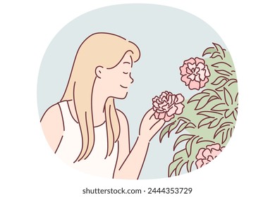 Woman enjoys scent of rose flowers by inhaling scent while walking in park or greenhouse. Fair-haired girl, closing eyes, sniffs buds of flowers growing on bushes and blooming in spring season