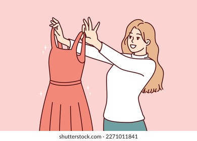 Woman examines beautiful evening dress choosing outfit for going to ball or festive party. Girl shopping in clothing store holds elegant dress from latest collection from famous fashion designer 