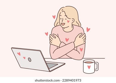 Woman exchanging romantic messages in laptops hugs herself rejoicing at received congratulations on valentine day. Girl who read romantic compliments in online correspondence smiles 