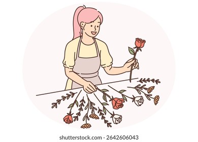 Woman florist stands near table with flowers collecting beautiful bouquet for wedding gift to bride. Girl in apron works as florist or is owner of small business for creating flowers for presents