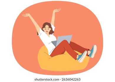Woman freelancer joyfully raises hands after completing work on project, sitting in soft ottoman with laptop on lap. Positive girl freelancer doing distance job or receiving online education