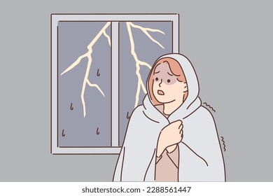 Woman was frightened by lightning and storm outside window wrapped herself in blanket because of fear of thunderstorm. GIrl suffers from phobia caused by bad weather and night hurricane