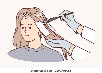 Woman getting hair dyed by professional hairdresser making stylish hairstyle for going to party. Hairdresser with brush for dyeing hair of client who applied for services in beauty salon 