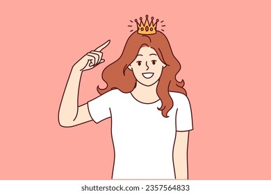 Woman with golden crown on head, smiling broadly and looking at screen, showing confidence and narcissism. Happy girl tries on princess crown and dreams of marrying prince or king.