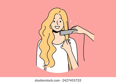 Woman at hairdresser appointment using hair straightener to straighten curls before party or date. Happy blonde girl visits hairdresser or stylist who helps change image and become more beautiful