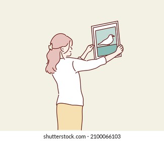 Mujer colgando marco de foto en blanco en una pared blanca. Ilustraciones de diseño vectorial de estilo dibujado a mano.