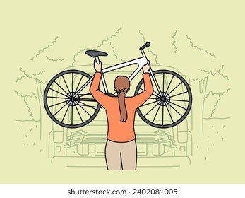 Woman hangs bicycle on pickup truck for trip to nature and active recreation during summer holidays. Young girl cyclist goes on trip and puts bicycle on stand in back of automobile