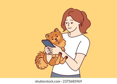 Woman has small dog and phone in hands, and is looking on internet for hotel or cafe to relax with pet. Caring girl with dog calls veterinarian to make appointment for vaccinations