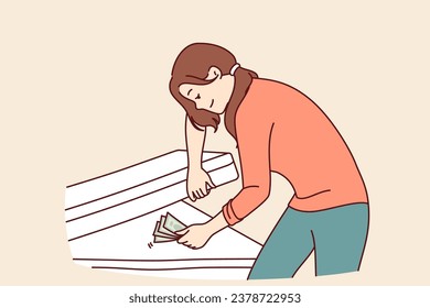 Woman hides money under mattress and smiles, keeping money safe and wanting to save up for big purchase. Concept of lack of financial literacy in girl who does not trust bank deposits