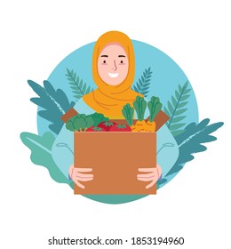 A woman in a hijab happily holds a cardboard box filled with fruit and vegetables