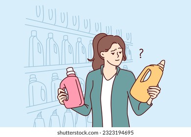 Una mujer sostiene botellas de detergente para lavar ropa o productos de limpieza cerca de estanterías en un supermercado. Chica visitante de un supermercado compara productos que eligen la mejor opción para la compra